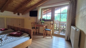 A bedroom with a bed, a desk, a chair, a radiator, and a window with a view of trees.