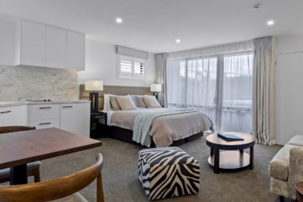 A modern hotel room with a bed, a small dining table, a sofa, and a round coffee table.