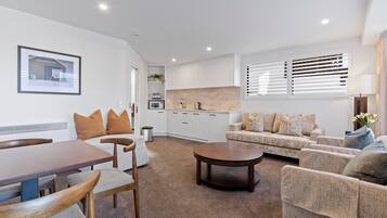 A modern living room with a dining table, sofa, and coffee table. There is a kitchen area with cabinets and a microwave.