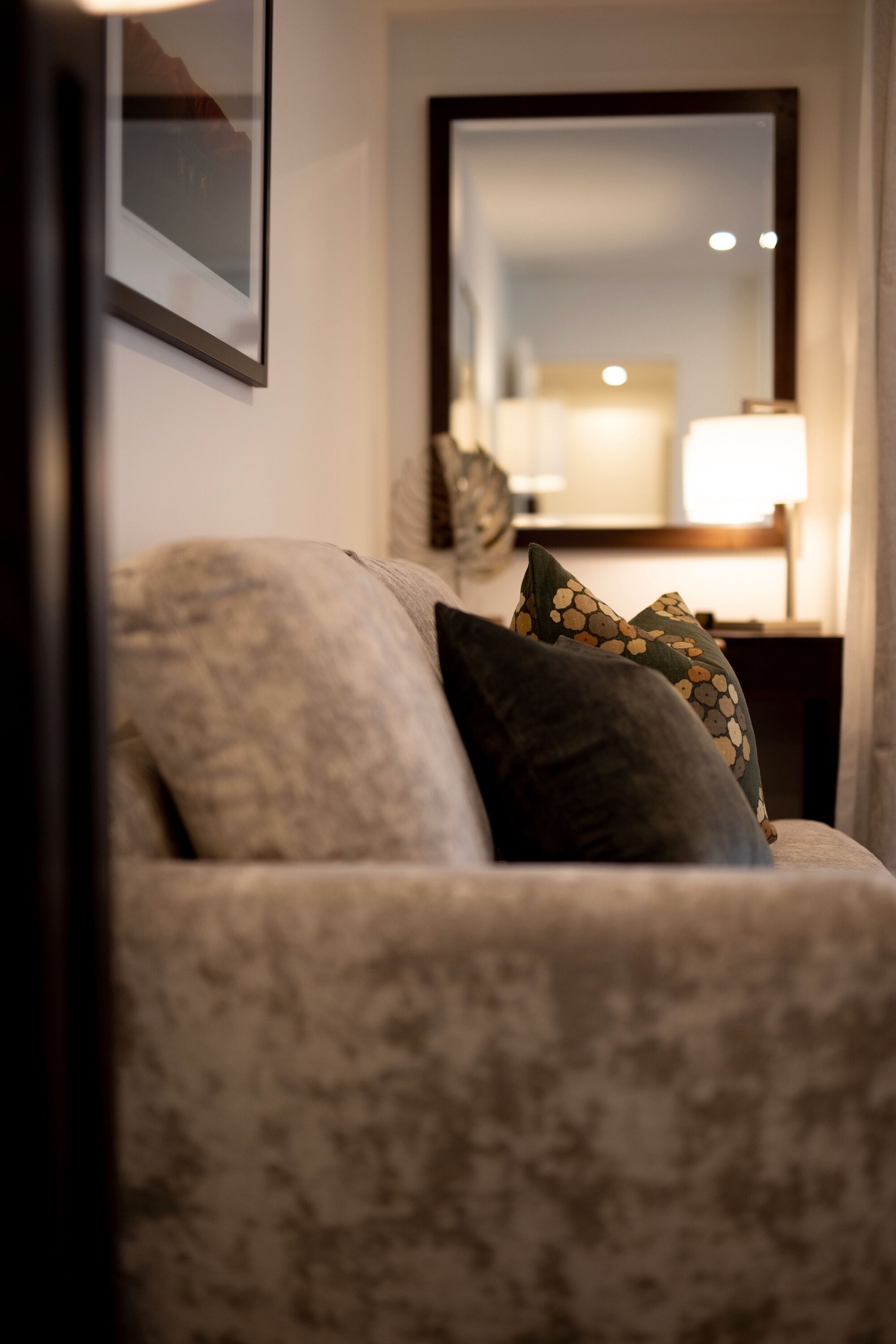 A living room with a sofa and pillows, a framed picture on the wall, and a lamp on a side table.