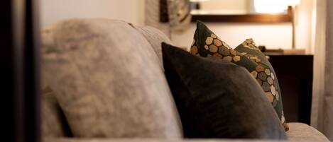 A living room with a sofa and pillows, a framed picture on the wall, and a lamp on a side table.