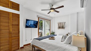 A bedroom with a bed, a ceiling fan, a TV mounted on the wall, and wooden shutters. - Charming condo walking to beach and town (Tamarindo)