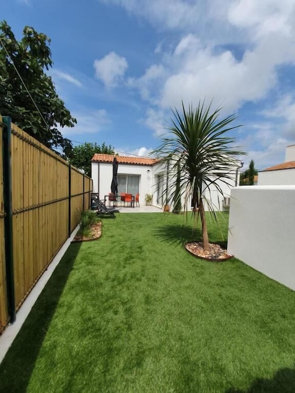 Un patio trasero bien cuidado, con un césped impecable, una valla de madera y una palmera.