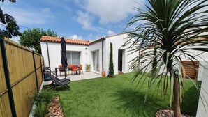 A backyard with a lawn, a wooden fence, a patio with a table and chairs, and a palm tree.