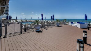 A rooftop pool area with lounge chairs, umbrellas, and a view of the ocean.