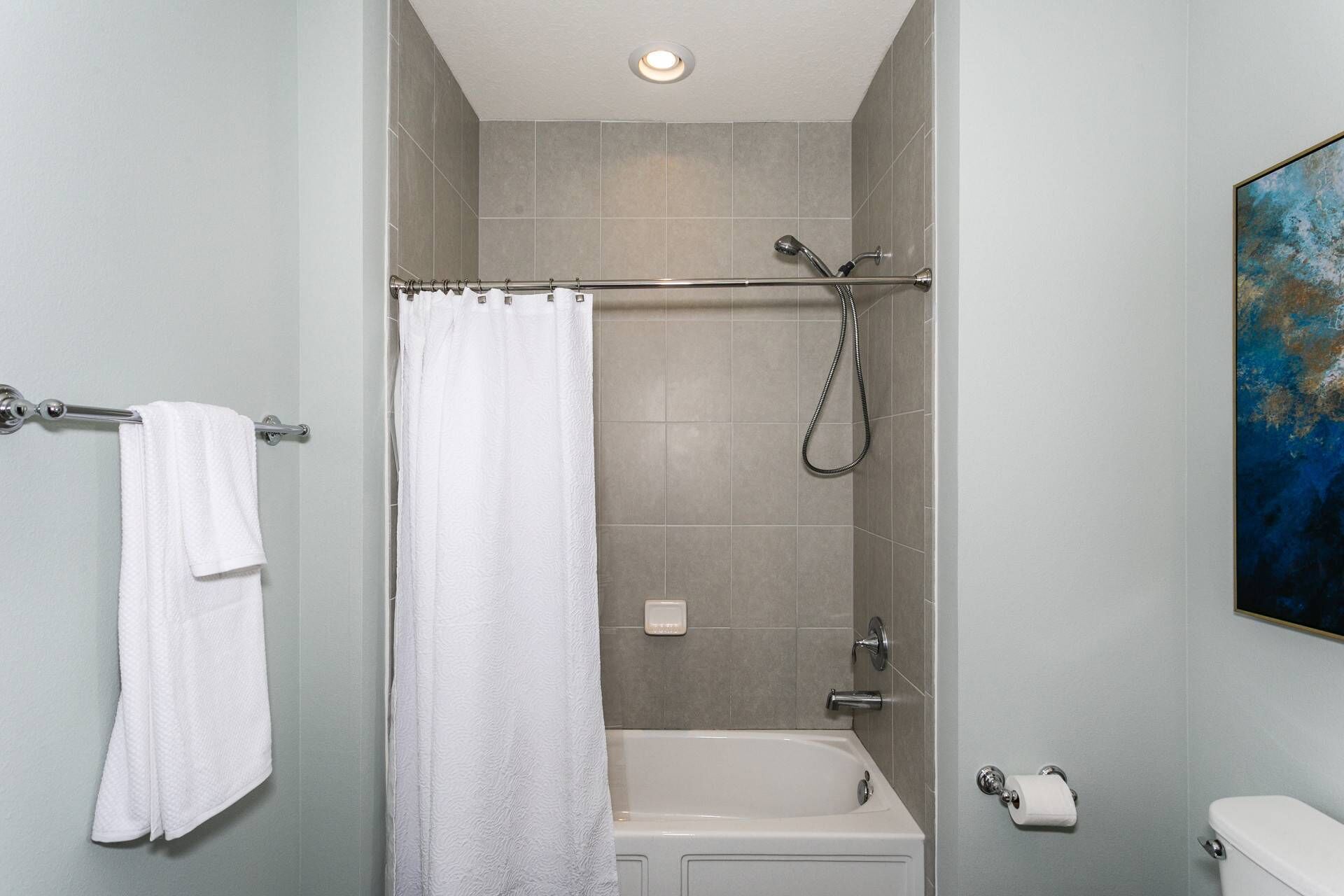 A bathroom with a shower, bathtub, toilet, and a towel rack with a white towel.