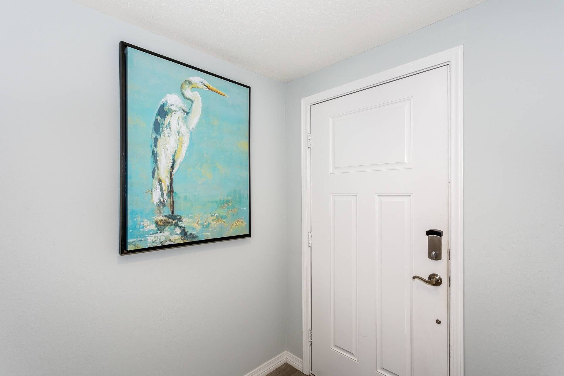 Un couloir avec une porte blanche et un tableau encadré représentant un oiseau, accroché au mur.