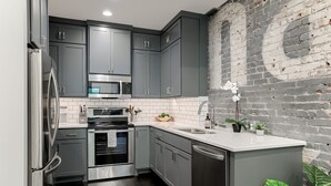 A modern kitchen with grey cabinets, stainless steel appliances, and a brick wall. - New Downtown Luxury Condo, by UNL, stadium & arena, above luxury retail #204 (Lincoln)
