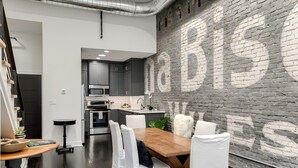 A modern kitchen with dark cabinets, a wooden dining table, and a brick wall with a large 'abuse' mural. - New Downtown Luxury Condo, by UNL, stadium & arena, above luxury retail #204 (Lincoln)