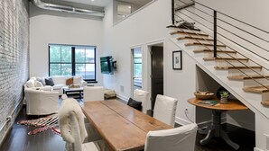 A modern living room with a wooden dining table, white sofas, and a staircase. - New Downtown Luxury Condo, by UNL, stadium & arena, above luxury retail #204 (Lincoln)