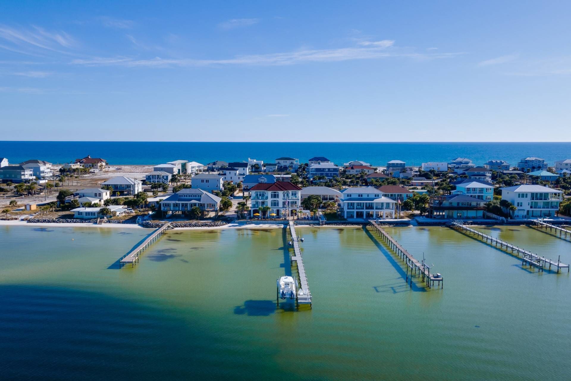 An aerial view of a coastal residential area with houses, a pier, and a clear blue sky.