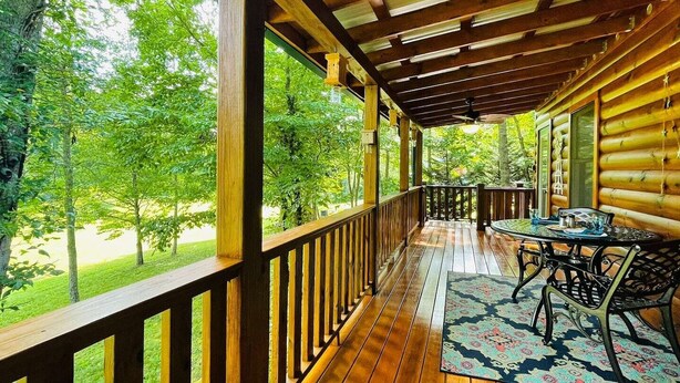 Una terraza de madera con barandilla, una mesa con sillas y vistas a un paisaje verde.