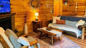 Un acogedor interior de cabaña de madera con chimenea, televisor, sofá y una mesa de centro.