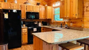 Cocina de cabaña de madera con un refrigerador negro, microondas, estufa, encimera de granito y gabinetes de madera.