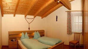 A bedroom with a wooden ceiling, a bed with green bedding, a nightstand, a chair, and a window with curtains. - Ruhig Gelegene Fewo 02 - Rustikal und Modern Eingerichtet in Waldnähe (Achslach / Lindenau)