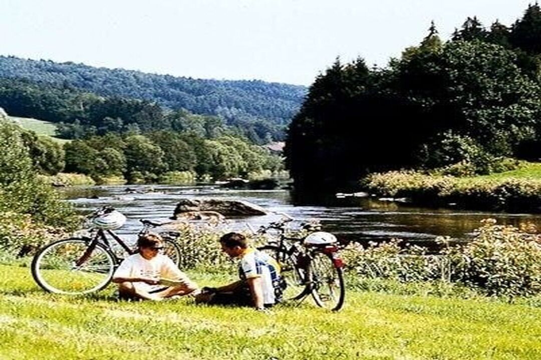 Two people sitting on grass near a river with bicycles.
