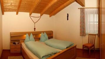 Une chambre avec un plafond en bois, un lit avec une literie verte, une table de chevet, une chaise et une fenêtre avec des rideaux.