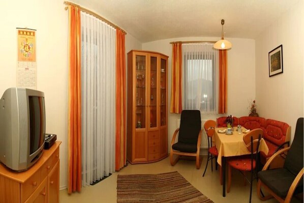 A dining area with a table and chairs, a television on a cabinet, and a cabinet with glass doors.