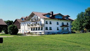 A large, white building with a red-tiled roof, multiple balconies, and a well-maintained lawn in front. - Ruhig Gelegene Fewo 07 - Rustikal und Modern Eingerichtet in Waldnähe (Achslach / Lindenau)