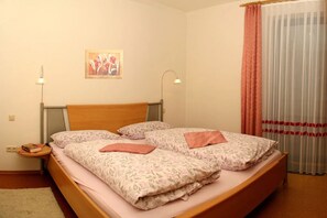 A double bed with floral bedding, a bedside table with a book, a lamp, and a painting on the wall.