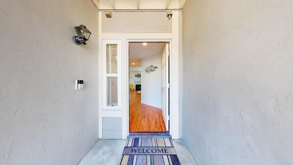 Un pasillo con felpudo, una puerta con ventana y una lámpara de pared.