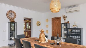 A dining area with a wooden table, chairs, a large wall clock, and a decorative pineapple centerpiece. - Wonderful and cheerful villa in Javea, Costa Blanca, Spain  with heated pool for 8 persons (Javea)