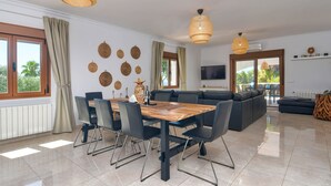 A modern living room with a dining area, large windows, and a TV mounted on the wall. - Wonderful and cheerful villa in Javea, Costa Blanca, Spain  with heated pool for 6 persons (Javea)