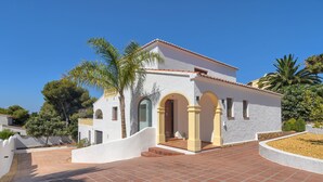 A white building with a red-tiled roof, arched doorways, and a paved driveway. - Wonderful and cheerful villa in Javea, Costa Blanca, Spain  with heated pool for 6 persons (Javea)
