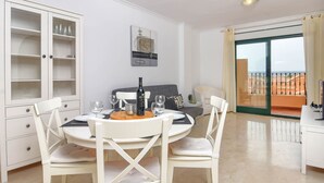 Un coin repas avec une table ronde et des chaises, un meuble avec des portes en verre, un canapé et une vue sur l’extérieur par une porte vitrée.