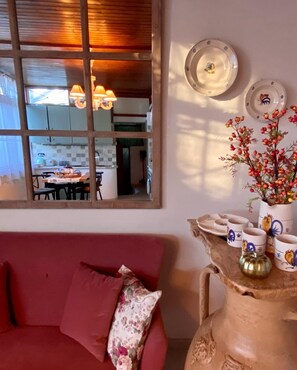 A cozy living room with a red sofa, a decorative vase with a plant, and a table with ceramic cups and plates.