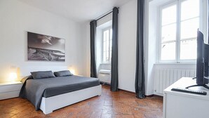 Ein Schlafzimmer mit einem Bett, einem Schreibtisch, einem Stuhl, einem Fenster und einem Bild an der Wand.