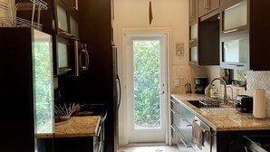 Una cocina moderna con armarios oscuros, electrodomésticos de acero inoxidable, encimera de mármol y vistas al exterior, donde se aprecia vegetación.
