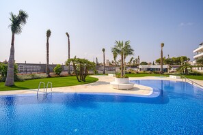 Una piscina con palme, un vaso bianco circolare e un edificio moderno sullo sfondo.