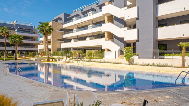 A modern building with a swimming pool, palm trees, and outdoor seating.