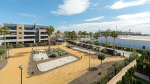 A modern building with multiple floors, a landscaped courtyard with palm trees, and a clear blue sky.