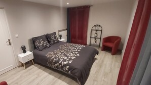 Een slaapkamer met een bed, nachtkastje, rode stoel en een metalen standaard met een spiegel.