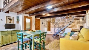 Un comedor con una mesa y sillas de madera, un televisor sobre un mueble, y una escalera que conduce a un nivel superior.
