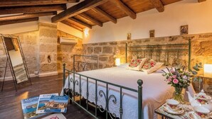 Un dormitorio rústico con pared de piedra, techo de madera, estructura de cama de metal y mesita de noche con un florero.