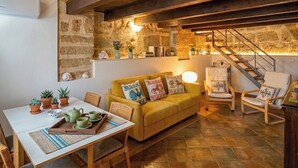 Una habitación acogedora con techo de madera, paredes de piedra, un sofá amarillo, una mesa de comedor con sillas y una escalera.