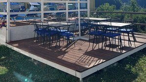 An outdoor seating area with tables and chairs, a covered pavilion, and a view of a mountain and a building in the background. - One-bedroom Apartment with Pool, Playground and breathtaking view (Piazza-Tralia-Pendolo)