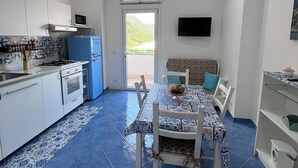 A compact kitchen with white cabinets, a blue refrigerator, and a dining area with a patterned tablecloth. - One-bedroom Apartment with Pool, Playground and breathtaking view (Piazza-Tralia-Pendolo)