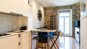 A compact kitchen with a stone wall, a dining area with two chairs, and a ladder leading to a balcony. - CASA NINA - Charming apartment with pool on the property (Porto)