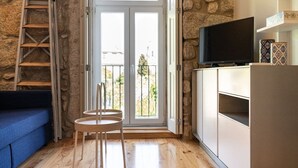 A cozy room with a stone wall, a wooden ladder, a blue sofa, two chairs, a television on a cabinet, and a balcony with a railing. - CASA NINA - Charming apartment with pool on the property (Porto)