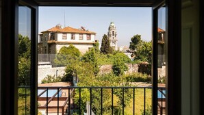 A view from a window overlooking a building with a bell tower, surrounded by greenery. - CASA NINA - Charming apartment with pool on the property (Porto)