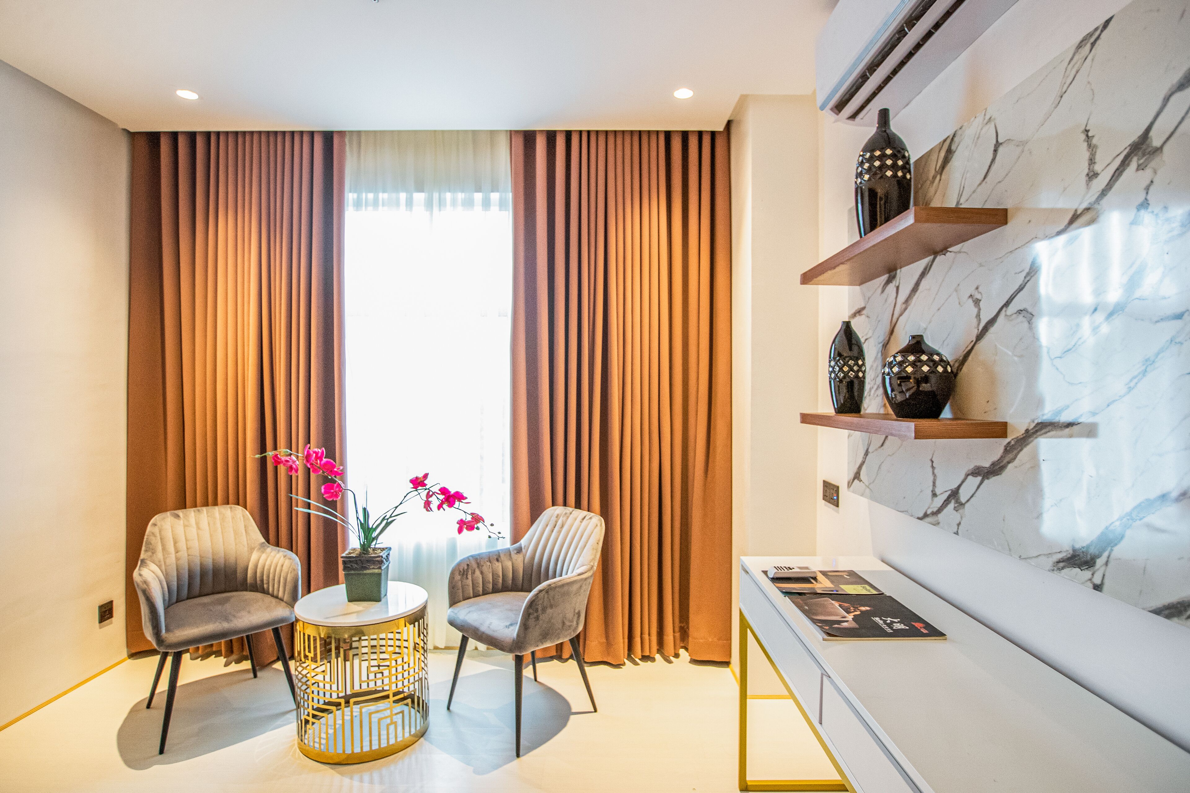 A modern room with two armchairs, a small round table with a vase of flowers, and a marble wall with shelves.