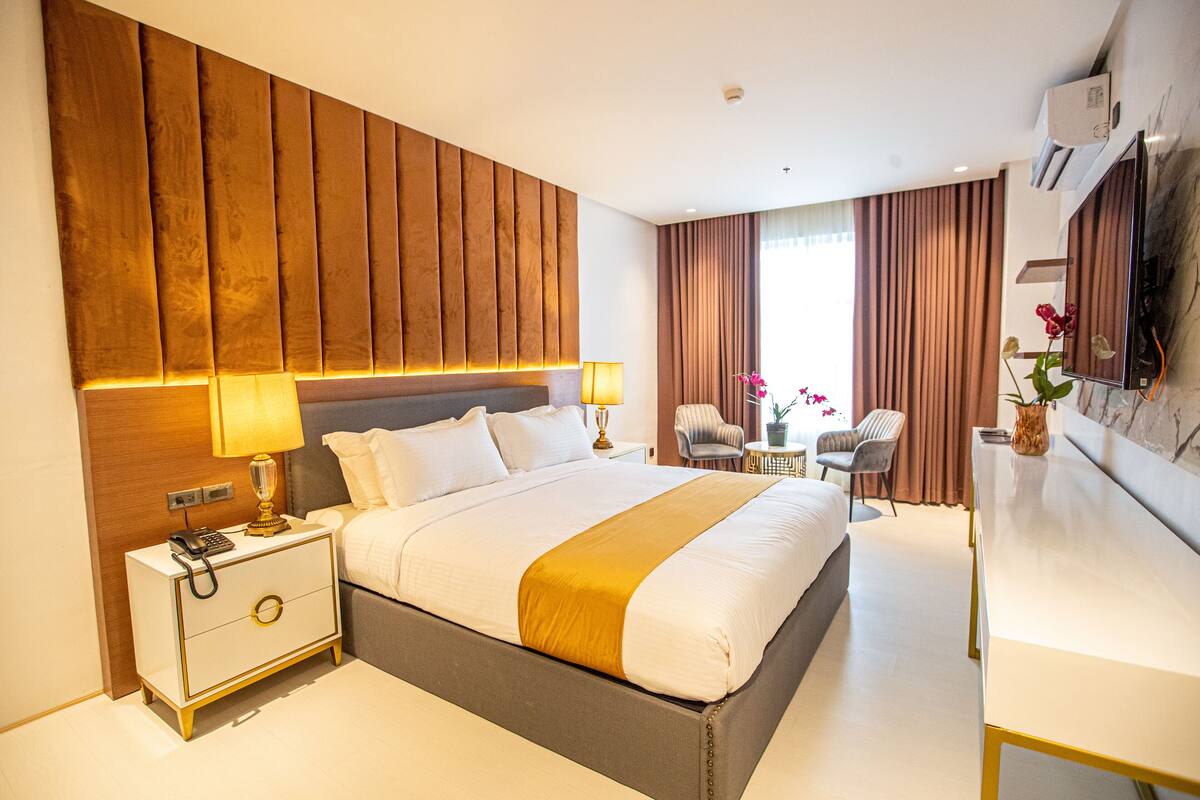 A modern hotel room with a large bed, bedside lamps, a desk, and a view of the city.