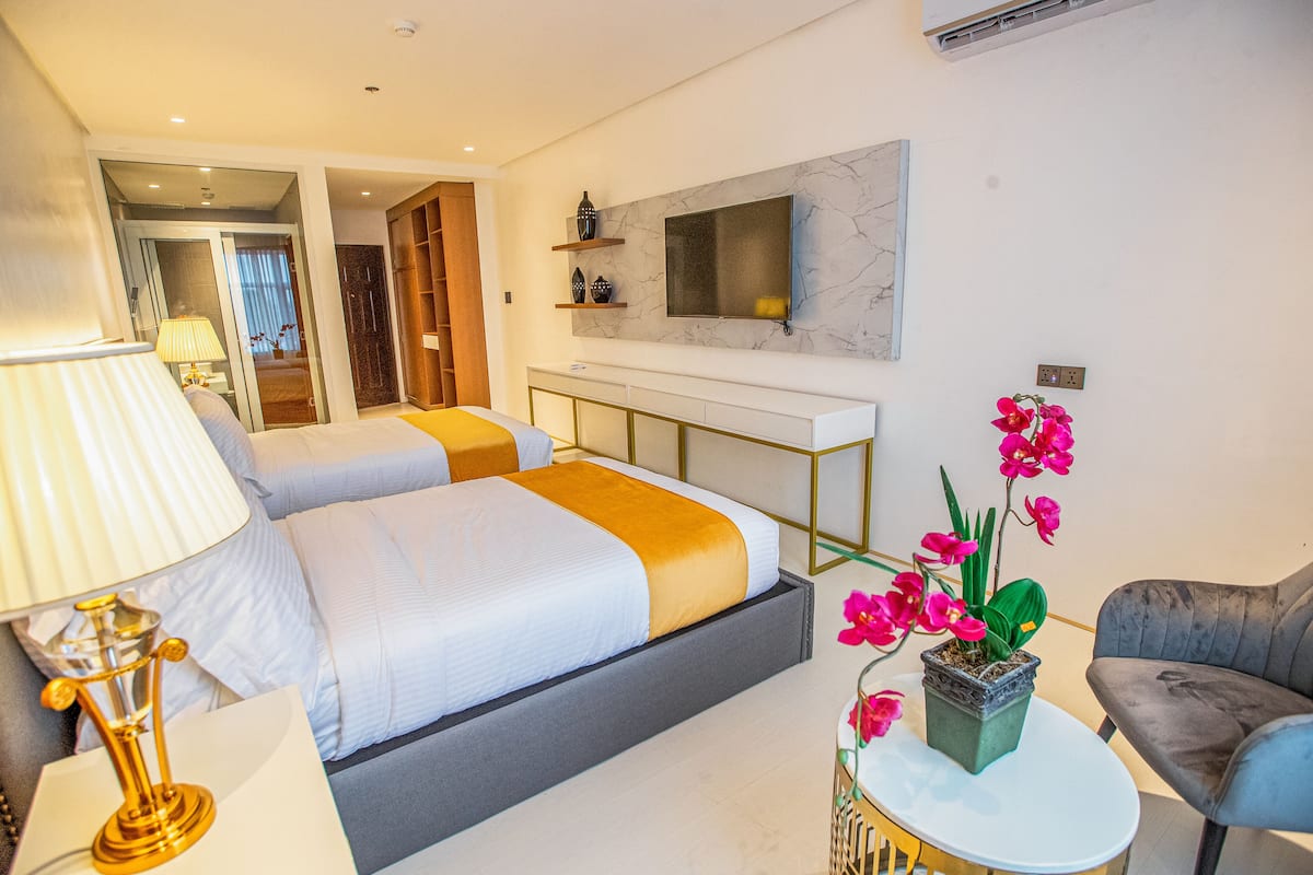 A modern hotel room with a bed, bedside table, lamp, TV, and a potted orchid.