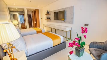 A modern hotel room with a bed, bedside table, lamp, TV, and a potted orchid.
