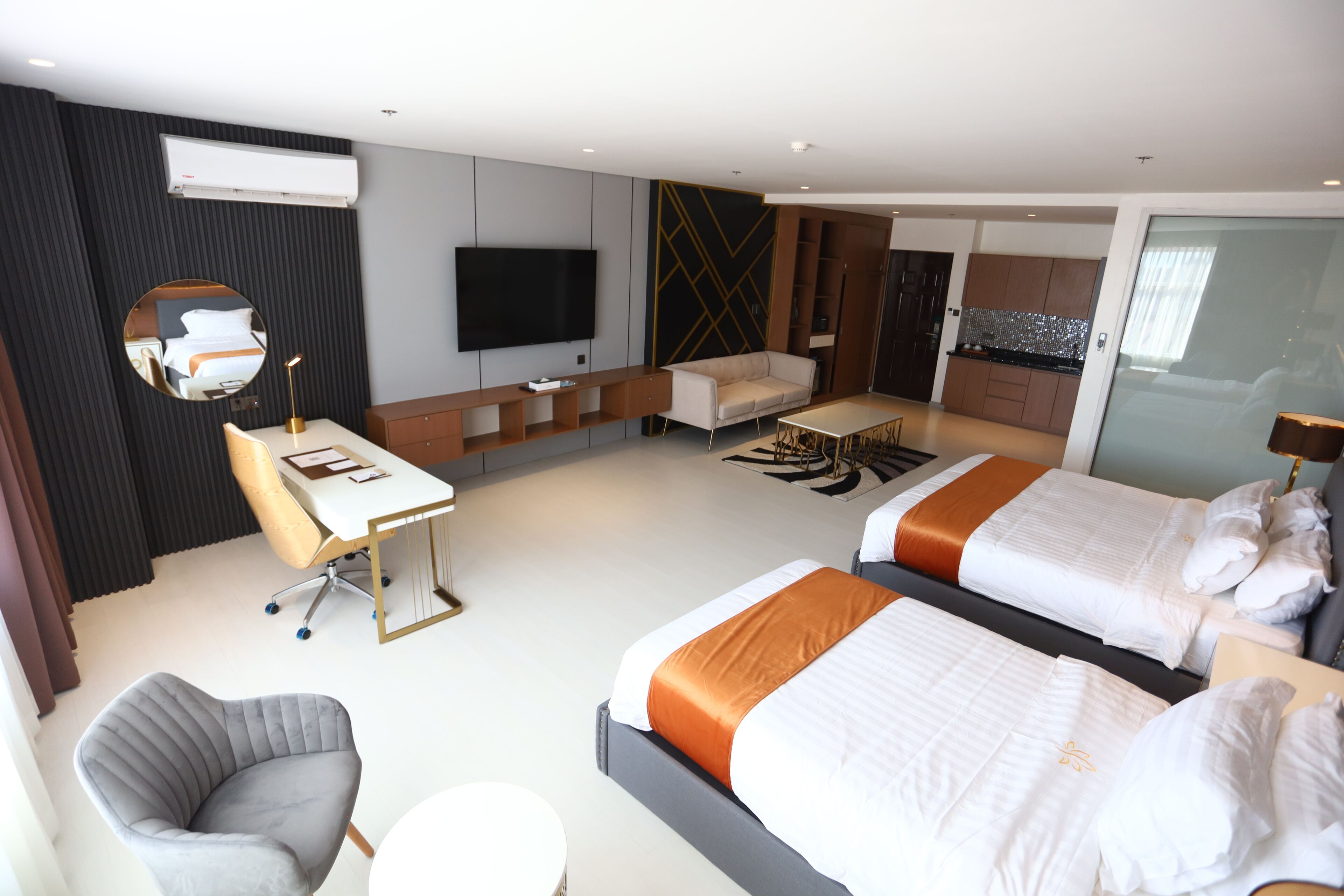 A modern hotel room with a large bed, a desk, a chair, a TV, and a kitchenette.