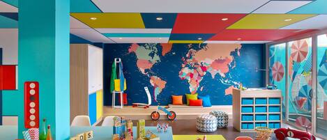 A brightly colored children's playroom with educational toys, a world map on the wall, and a window with a view of the sea.